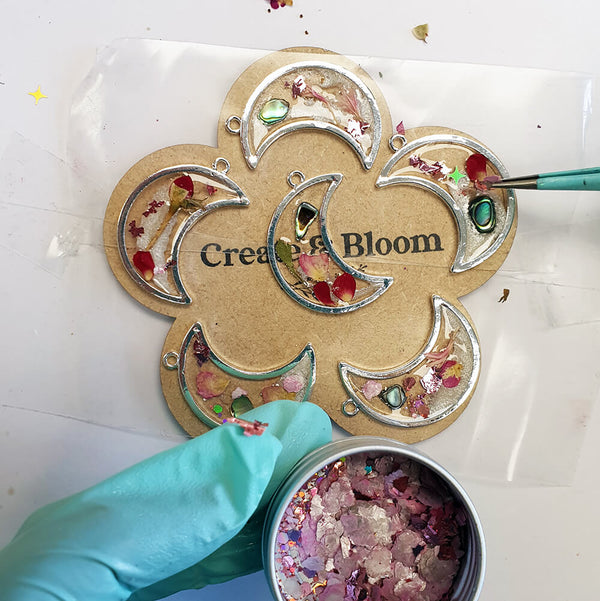 Decorative resin pendants with 'Create & Bloom' text on a white surface.