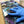 A hand wearing a blue nitrile glove smooths a glossy, colorful resin art board with a galaxy design. A bottle of Apex Resin CurePro resin is visible in the background on a table with other crafting supplies.